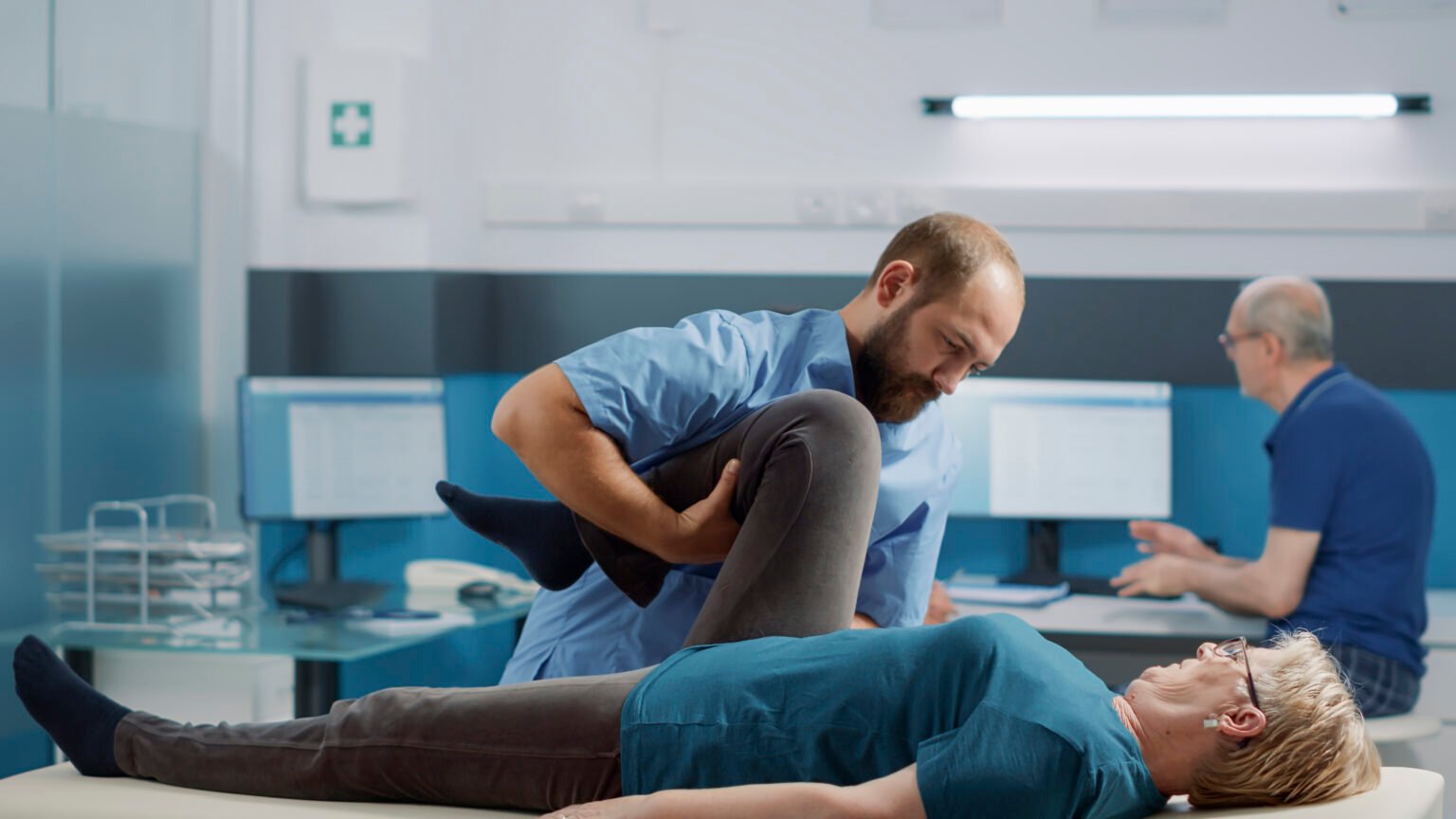 Medical specialist helping elder patient to cure physical injury with bones cracking procedure, stretching legs muscles in office. Therapist using alternative medicine to increase mobility.